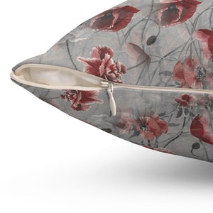 May include: A decorative pillow with a floral pattern featuring red poppies on a gray background. The pillow has a zipper closure and is designed for home decor.