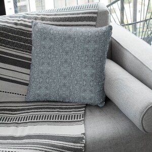 May include: A gray couch with a gray and white striped throw blanket and a blue throw pillow. The couch is in a living room setting.