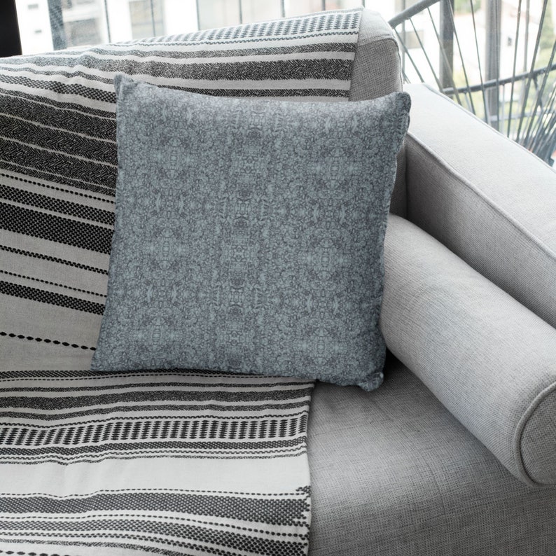 May include: A gray couch with a gray and white striped throw blanket and a blue throw pillow. The couch is in a living room setting.