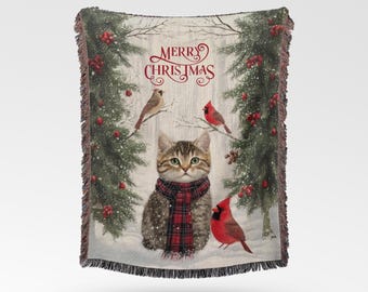 May include: A woven throw blanket featuring a tabby cat wearing a red and black plaid scarf, surrounded by snowy pine trees with red berries and cardinals. The text Merry Christmas is printed in red script at the top of the blanket.