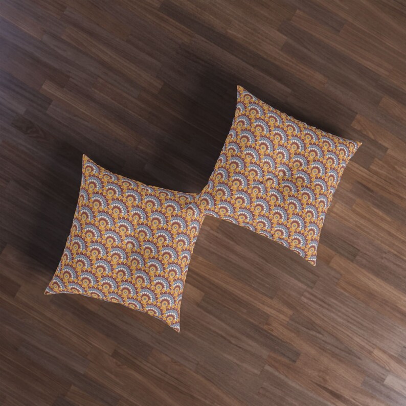 May include: Two square throw pillows with a geometric pattern of yellow, orange, and blue. The pillows are on a wood floor.