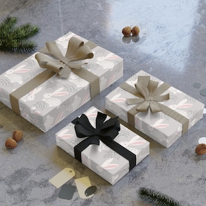 May include: Three gift boxes wrapped in gray paper with a white bunny pattern. The boxes are tied with brown and black ribbon.