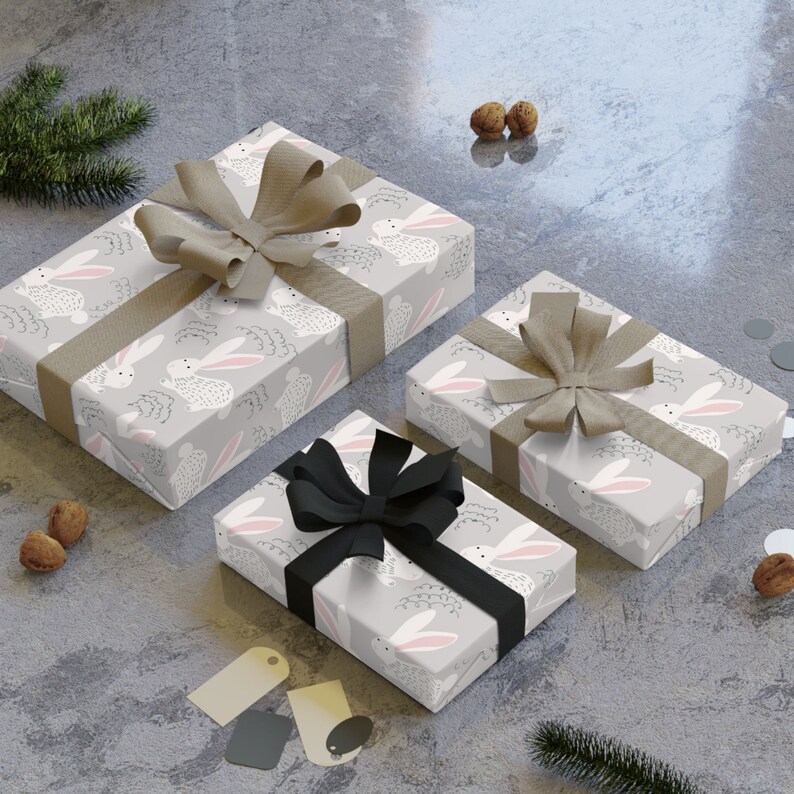 May include: Three gift boxes wrapped in gray paper with a white bunny pattern. The boxes are tied with brown and black ribbon.