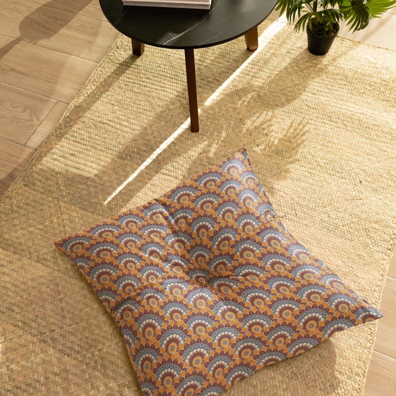 May include: A large, square floor cushion with a colorful geometric pattern in shades of orange, brown, blue, and white. The cushion is made of fabric and has a tufted button in the center.