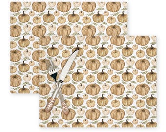 May include: Two brown and white watercolour pumpkin patterned placemats with a fork and knife on top.