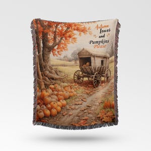 May include: Woven throw blanket featuring a fall scene with pumpkins, a wooden wagon, and a large tree with orange leaves. The text "Autumn Leaves and Pumpkins Please" is printed on the blanket. The blanket has a fringed edge.