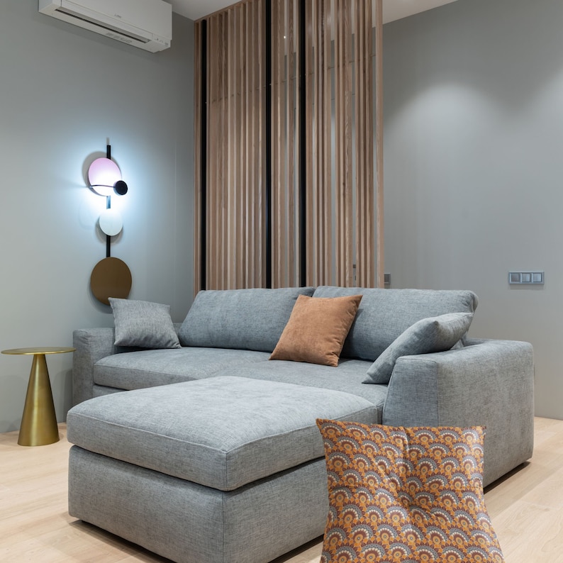 May include: A gray sectional sofa with a light gray ottoman and a brown throw pillow. The sofa is in a living room with a wooden slat wall behind it.