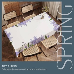Peut inclure: Une nappe blanche avec un motif floral de fleurs violettes et de feuilles vertes. La nappe est sur une table en bois avec quatre chaises. Le texte "SPRING" est dans le coin sup&eacute;rieur droit de l'image. Le texte "JOY RISING" est dans le coin inf&eacute;rieur gauche de l'image. Le texte "Celebrate the season with style and enthusiasm" est sous le texte "JOY RISING".