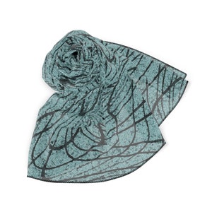 May include: A teal blue scarf with a black and white abstract pattern. The scarf is rolled up and has a black trim.