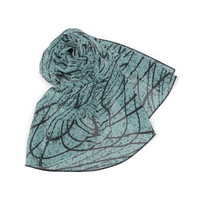 May include: A teal blue scarf with a black and white abstract pattern. The scarf is rolled up and has a black trim.