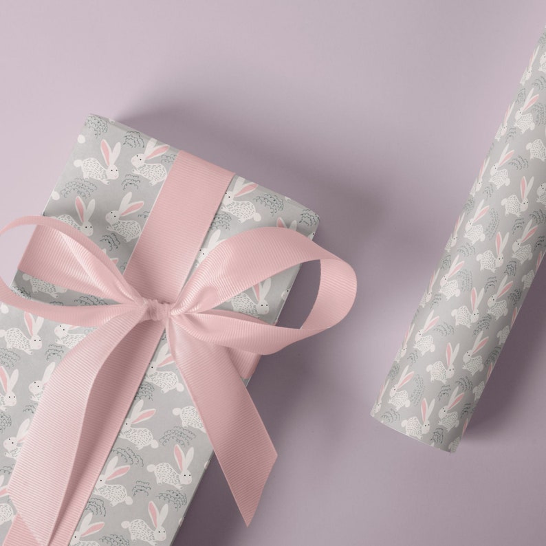 May include: A gift box wrapped in gray wrapping paper with a white bunny rabbit pattern. The box is tied with a pink satin ribbon.