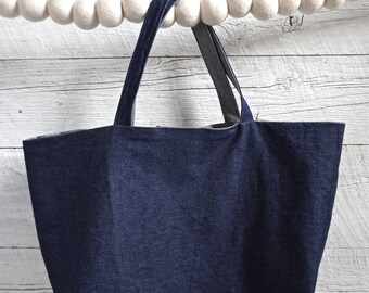 May include: A dark blue denim tote bag with a white background. The bag has two straps and is hanging from a white garland.