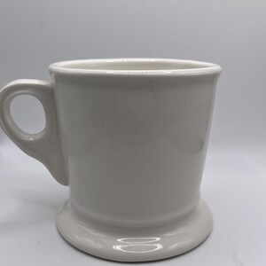 Puede incluir: Una taza de cer&aacute;mica blanca con base redondeada y asa. La taza tiene un dise&ntilde;o sencillo y cl&aacute;sico y es adecuada para caf&eacute;, t&eacute; u otras bebidas. La taza est&aacute; limpia y parece sin usar.