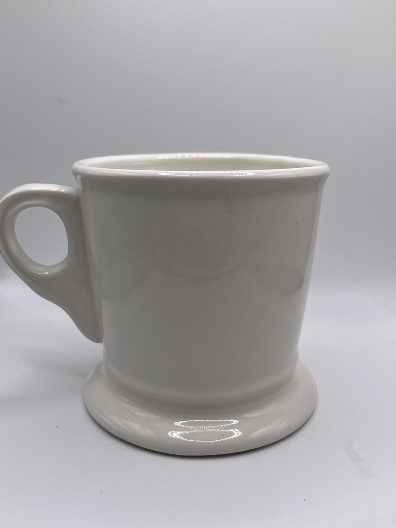 Puede incluir: Una taza de cer&aacute;mica blanca con base redondeada y asa. La taza tiene un dise&ntilde;o sencillo y cl&aacute;sico y es adecuada para caf&eacute;, t&eacute; u otras bebidas. La taza est&aacute; limpia y parece sin usar.