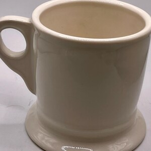 May include: A white ceramic mug with a black handle and the text "But First, Coffee" in a bold, black font. The mug is set against a blurred background, suggesting a cozy setting.