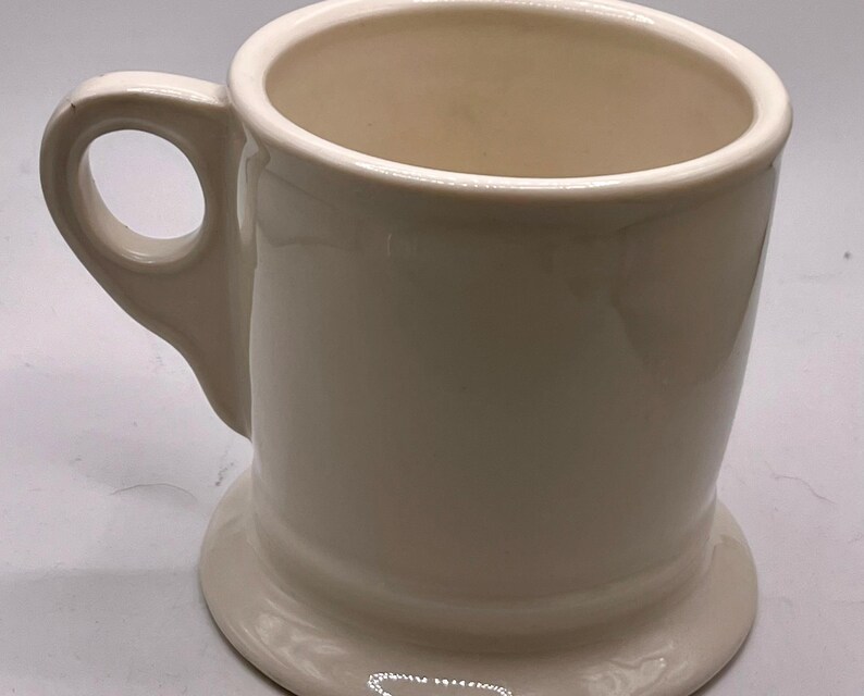 May include: A white ceramic mug with a black handle and the text "But First, Coffee" in a bold, black font. The mug is set against a blurred background, suggesting a cozy setting.