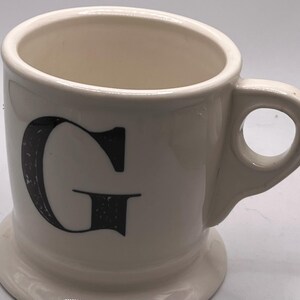 May include: A set of three ceramic mugs with a speckled, matte finish. Each mug features a different color: light blue, cream, and gray. The mugs have a simple, modern design and a comfortable handle.