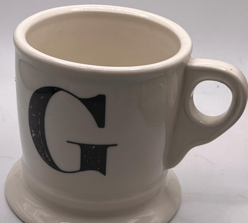 May include: A set of three ceramic mugs with a speckled, matte finish. Each mug features a different color: light blue, cream, and gray. The mugs have a simple, modern design and a comfortable handle.