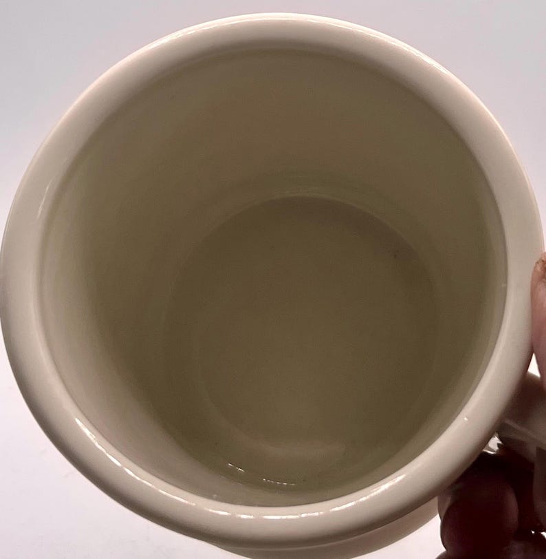 May include: Cream-colored ceramic mug with a rounded interior and a white exterior. The mug has a simple, classic design, suitable for hot beverages. The handle is visible on the right side of the mug.