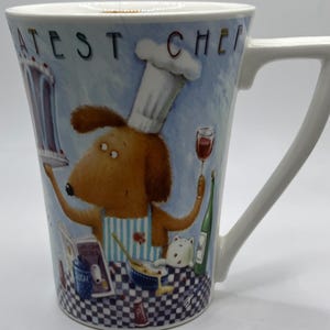 May include: White ceramic mug with a cartoon dog wearing a chef's hat and holding a cake. The mug has the text "Greatest Chef" on it.