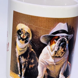 Könnte beinhalten: Weißer Keramikbecher mit einer Illustration einer Katze und einer Bulldogge. Die Katze trägt einen gelben Hut und ein Halstuch, während die Bulldogge einen grauen Hut trägt. Der Hintergrund ist braun.