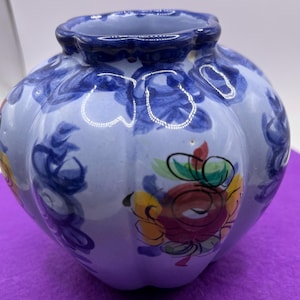 May include: A small, blue and white ceramic vase with a scalloped rim and a floral design. The vase is decorated with blue, yellow, red, and green flowers.