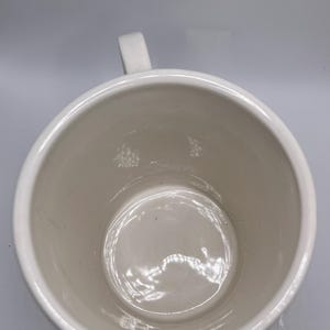 Puede incluir: Una taza de cer&aacute;mica blanca con cuerpo redondeado y asa. El interior de la taza es de color crema claro. La taza est&aacute; vac&iacute;a y parece limpia.