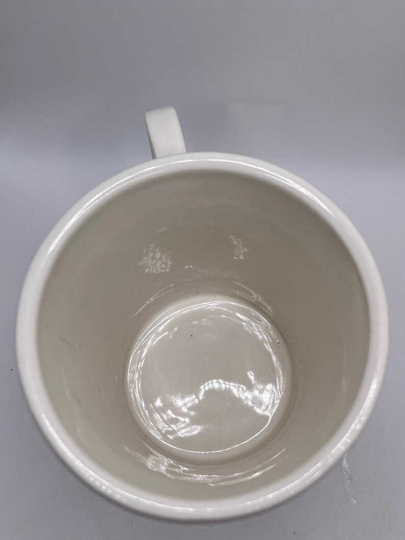 Puede incluir: Una taza de cer&aacute;mica blanca con cuerpo redondeado y asa. El interior de la taza es de color crema claro. La taza est&aacute; vac&iacute;a y parece limpia.