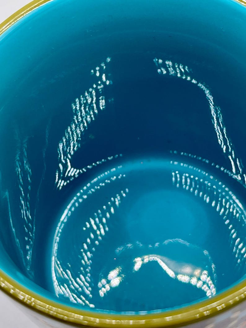 May include: Close-up of a teal-colored vessel with a gold rim. The interior of the vessel has a glossy finish with white, textured patterns. The gold rim adds a contrasting accent to the teal color.