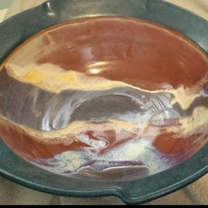 Puede incluir: Un cuenco de cerámica hecho a mano con un borde verde oscuro y un centro que presenta una mezcla de tonos marrones, blancos y amarillos. El interior del cuenco tiene un acabado brillante, creando una pieza artística única.