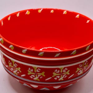 Puede incluir: Un cuenco de cer&aacute;mica rojo brillante con un patr&oacute;n decorativo. El cuenco presenta un interior rojo brillante y un exterior estampado con detalles en blanco, amarillo y azul. El borde est&aacute; adornado con detalles amarillos y blancos.