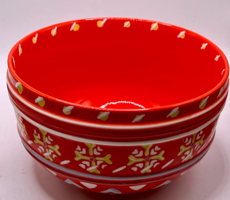 Puede incluir: Un cuenco de cer&aacute;mica rojo brillante con un patr&oacute;n decorativo. El cuenco presenta un interior rojo brillante y un exterior estampado con detalles en blanco, amarillo y azul. El borde est&aacute; adornado con detalles amarillos y blancos.
