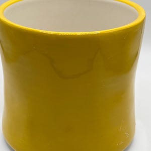 Puede incluir: Una taza de cer&aacute;mica amarilla con acabado brillante. La taza tiene forma cil&iacute;ndrica con un borde ligeramente ensanchado y un interior color crema. El exterior es de color amarillo brillante.