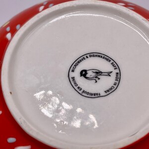 Puede incluir: Un cuenco de cer&aacute;mica rojo con lunares blancos y azules. La base del cuenco es blanca con un sello circular negro que dice "MICROONDAS Y LAVAVAJILLAS" y "HECHO EN CHINA". Una ilustraci&oacute;n de un p&aacute;jaro est&aacute; en el centro.