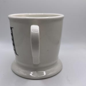 Puede incluir: Taza de cer&aacute;mica blanca con base redondeada y asa. La taza tiene un dise&ntilde;o de letras negras en el lateral. La taza est&aacute; dise&ntilde;ada para bebidas.