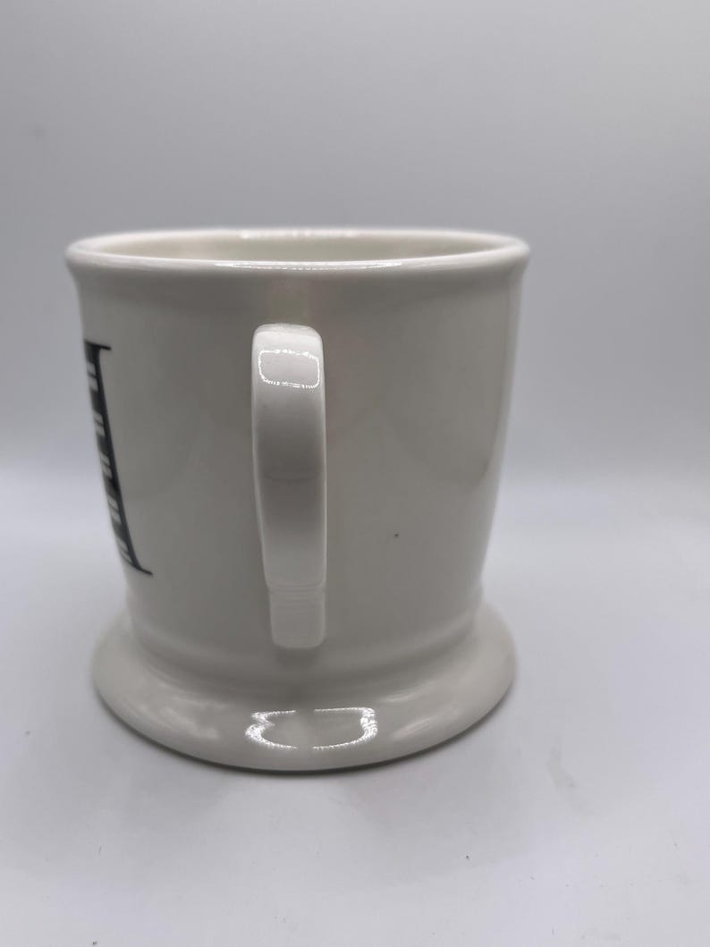 Puede incluir: Taza de cer&aacute;mica blanca con base redondeada y asa. La taza tiene un dise&ntilde;o de letras negras en el lateral. La taza est&aacute; dise&ntilde;ada para bebidas.
