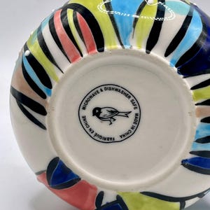 Może przedstawiać: Ceramiczny wazon z kolorowym, abstrakcyjnym wzorem. Wazon ma białą podstawę z wzorem niebieskich, ż&oacute;łtych, czerwonych i czarnych kształt&oacute;w. Na spodzie wazonu znajduje się napis "Microwave & Dishwasher Safe Made in China".