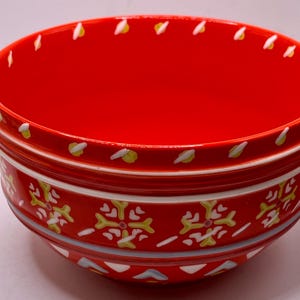 Puede incluir: Un cuenco de cer&aacute;mica rojo vibrante con un dise&ntilde;o decorativo. El cuenco presenta un interior y exterior rojos con detalles en blanco, amarillo y azul. El exterior tiene un patr&oacute;n repetitivo en forma de copo de nieve. El borde est&aacute; adornado con dise&ntilde;os blancos y amarillos en forma de hoja.