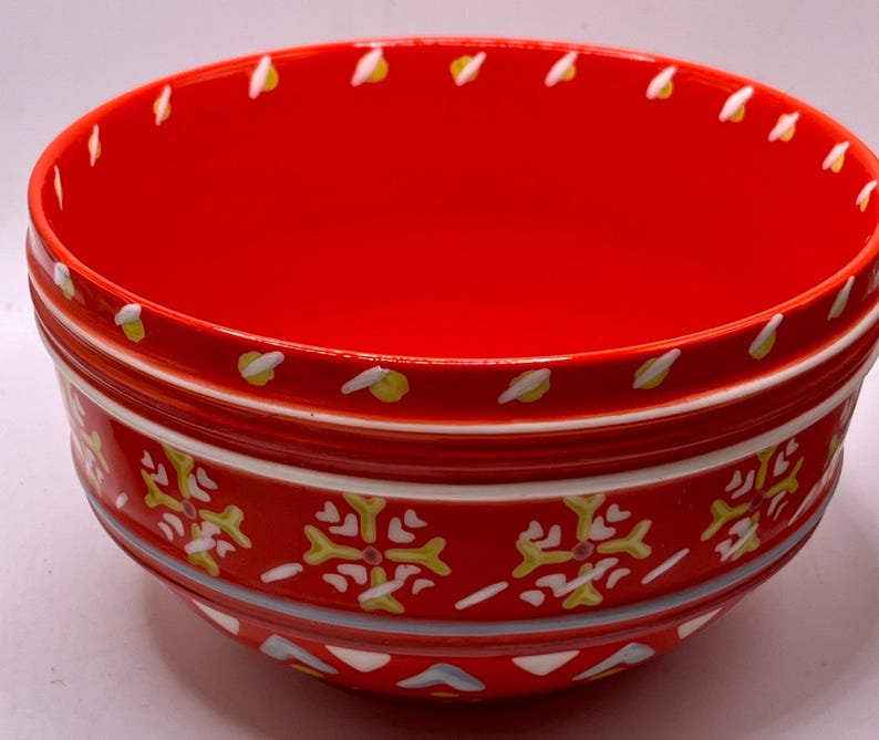 Puede incluir: Un cuenco de cer&aacute;mica rojo vibrante con un dise&ntilde;o decorativo. El cuenco presenta un interior y exterior rojos con detalles en blanco, amarillo y azul. El exterior tiene un patr&oacute;n repetitivo en forma de copo de nieve. El borde est&aacute; adornado con dise&ntilde;os blancos y amarillos en forma de hoja.