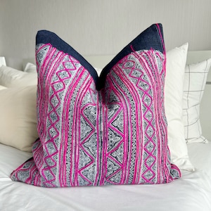 May include: A decorative pillow with a black background and a pink and white geometric pattern. The pillow is made of a soft, textured fabric and has a unique, hand-stitched design.