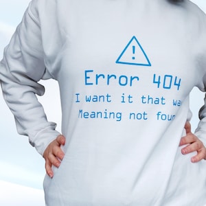 May include: White sweatshirt featuring the text "Error 404 I want it that way Meaning not found" in blue. A blue triangle with an exclamation mark is above the text. The sweatshirt has long sleeves.