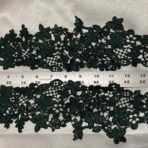 May include: Dark green floral lace trim with a delicate openwork design. The trim is approximately 16 inches long, with a ruler for scale. Perfect for embellishing garments or crafts.