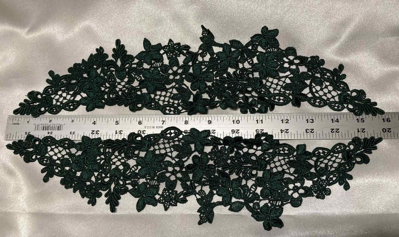 May include: Dark green floral lace trim with a delicate openwork design. The trim is approximately 16 inches long, with a ruler for scale. Perfect for embellishing garments or crafts.