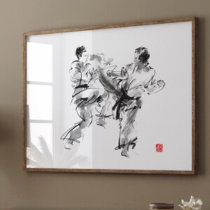 May include: A black and white ink drawing of two people in a martial arts pose. The drawing is framed and hanging on a wall above a wooden shelf with various items on it.