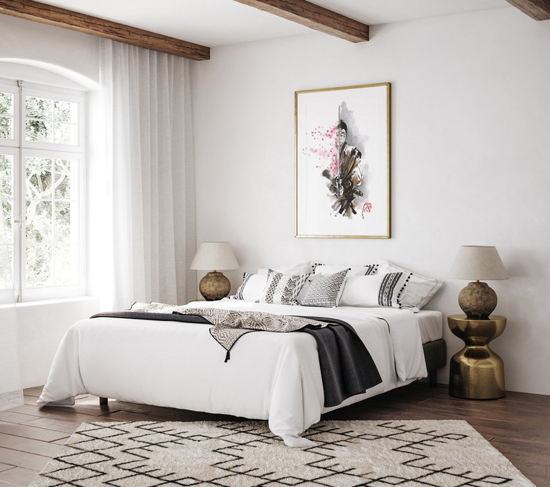 May include: A bedroom scene featuring a large white bed with decorative pillows and a dark gray throw blanket. A framed artwork with a gold frame hangs above the bed. The room has a neutral color palette with a patterned rug.