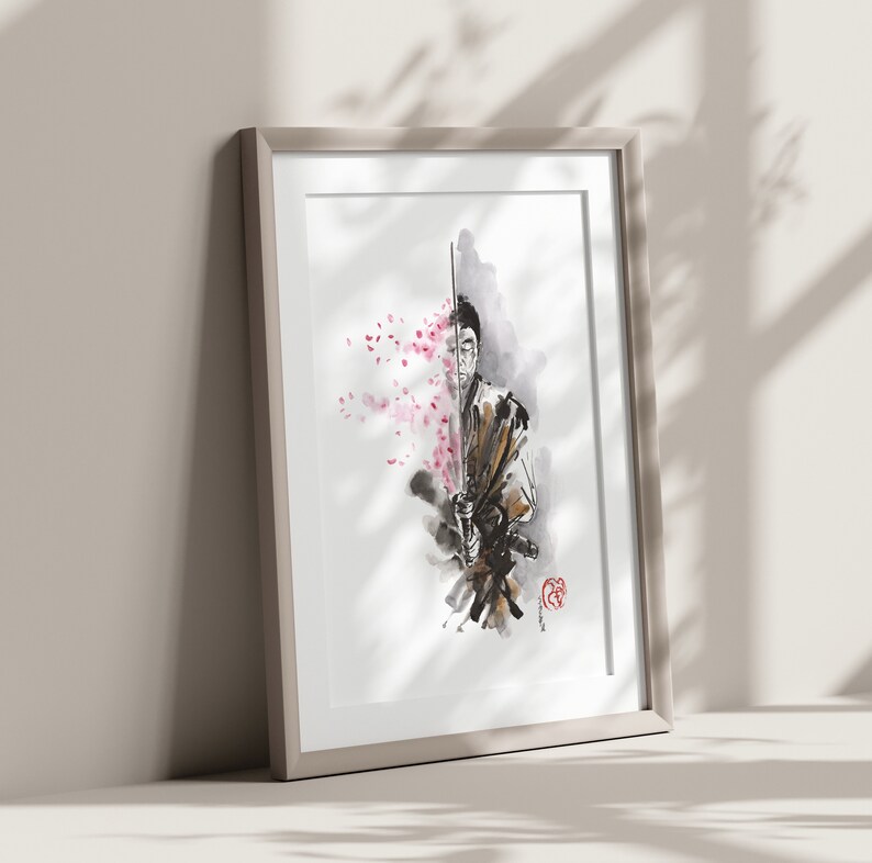 May include: Framed artwork featuring a watercolor illustration of a samurai holding a sword. The artwork is in shades of black, brown, and white, with pink cherry blossoms on the left side. The frame is a light beige color.
