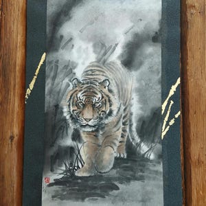 May include: A watercolor painting of a tiger walking forward, with a black and gray background. The tiger is brown and black with stripes. The painting is on a scroll with gold accents.