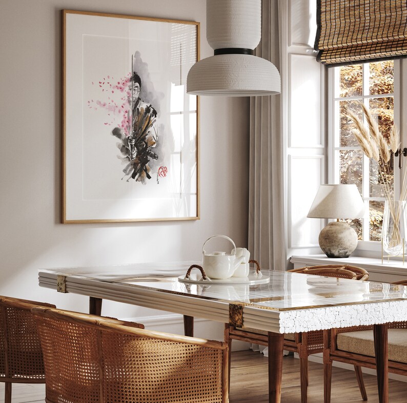 May include: A framed artwork depicts a samurai with a sword, rendered in watercolor with pink cherry blossoms. The artwork hangs above a dining table with a white marble top and rattan chairs. A white pendant light and a window with a bamboo shade are also visible.