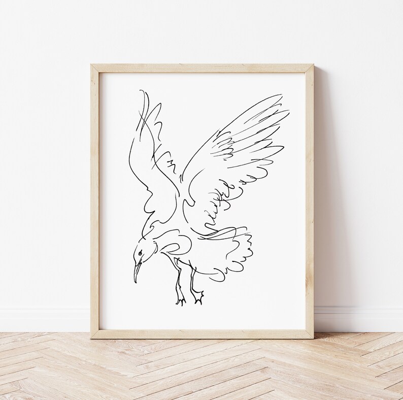 May include: A framed art print featuring a minimalist black line drawing of a seagull in flight. The bird is depicted with outstretched wings and a downward gaze, set against a white background. The frame is a light wood color.
