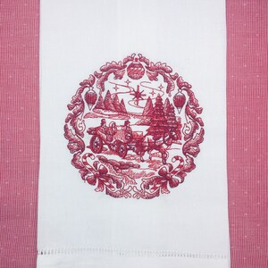 May include: A white tea towel with a red embroidered design of a winter scene with a horse-drawn carriage, trees, and a star. The design is surrounded by a decorative border.